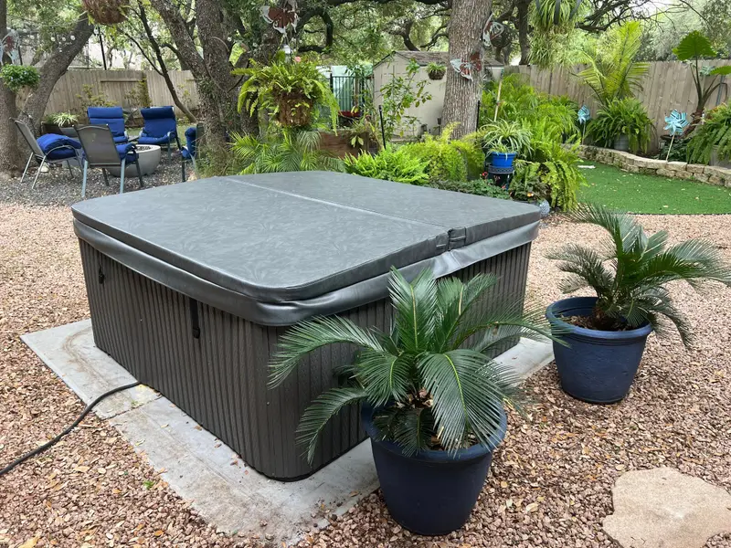 A grey hot tub cover on a tub in a shaded Texas backyard